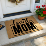 Loved Mom coir doormat featuring a natural brown fiber texture with bold black lettering and a small heart icon, creating a welcoming front porch entrance that celebrates motherhood with a stylish and durable outdoor floor mat