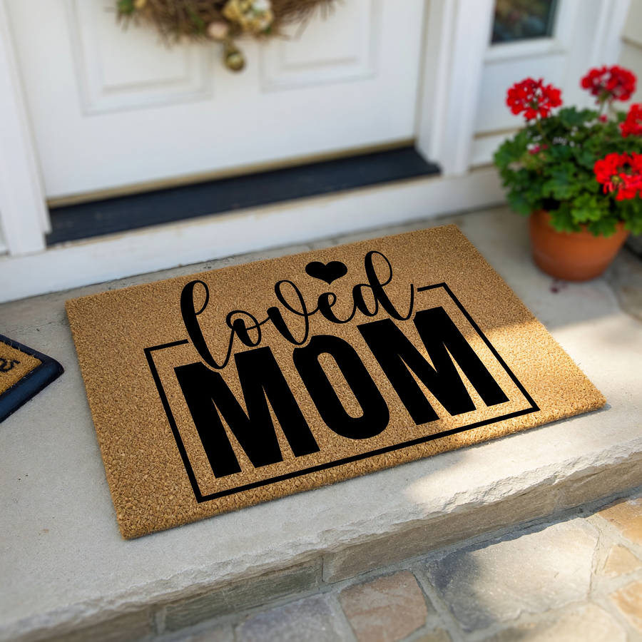 Loved Mom coir doormat featuring a natural brown fiber texture with bold black lettering and a small heart icon, creating a welcoming front porch entrance that celebrates motherhood with a stylish and durable outdoor floor mat